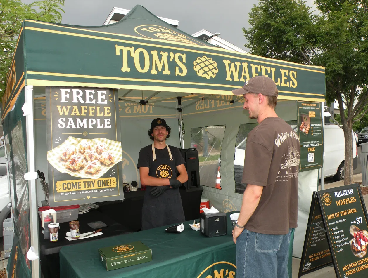 Tom's Waffles branded tent setup with staff member serving a customer at a Denver outdoor event