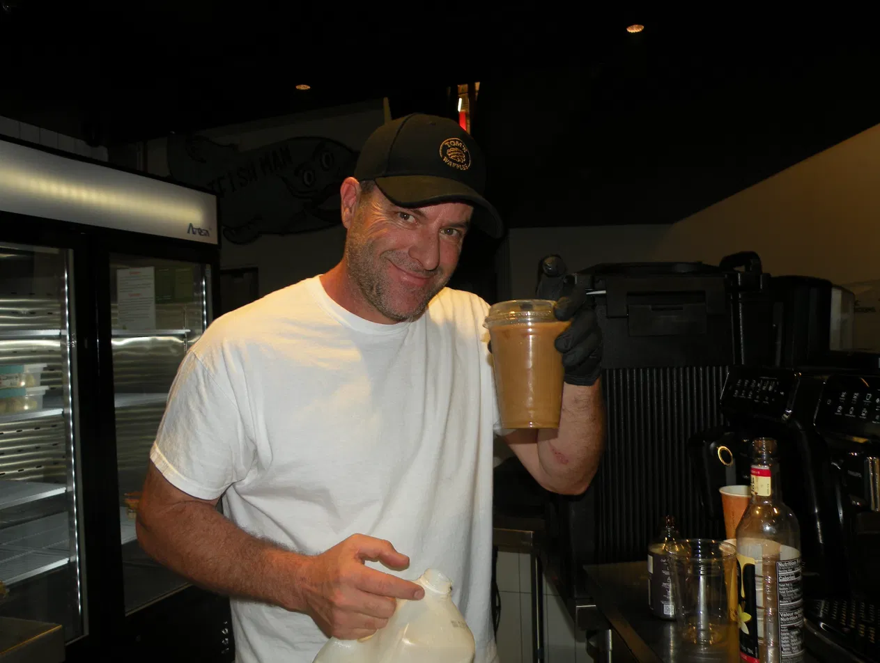 Tom's Waffles team member holding a freshly made iced latte at the espresso bar station