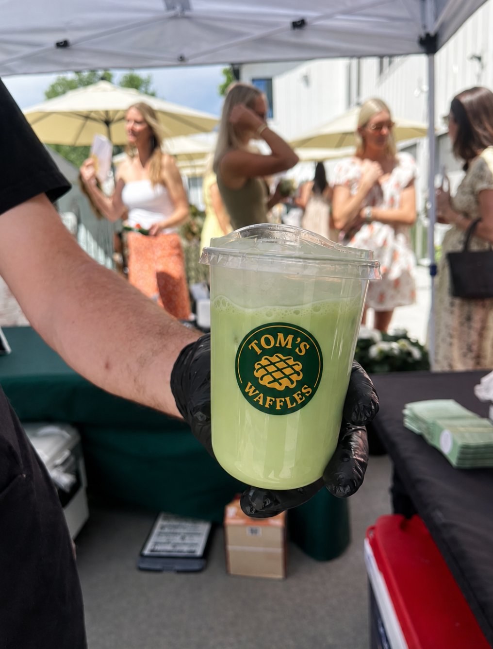 Fresh matcha latte with the Tom's Waffles logo at a Denver event