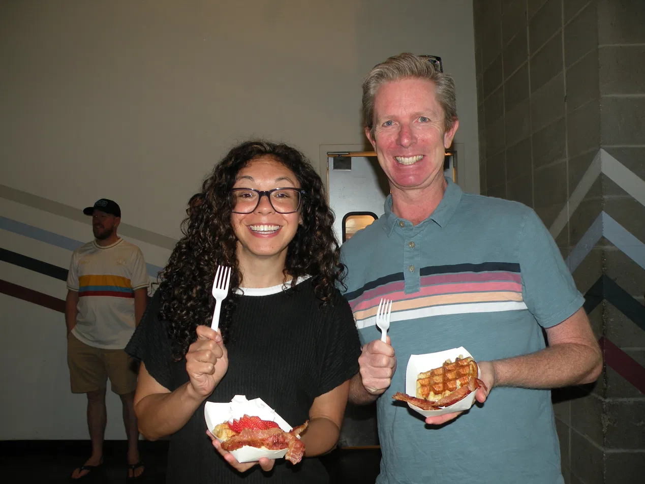Guests smiling and enjoying fresh Belgian waffles with bacon at a Denver wedding catered by Tom's Waffles