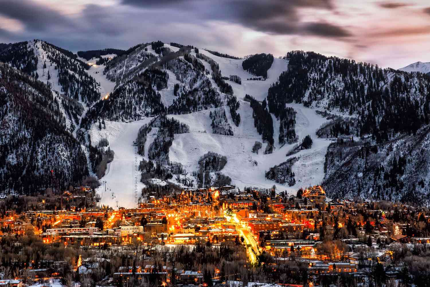 Aspen, Colorado mountain town at dusk with illuminated ski slopes and resort lights