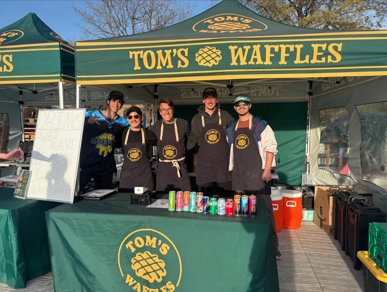 Five of our crew in aprons behind the Tom's Waffles table under the tent