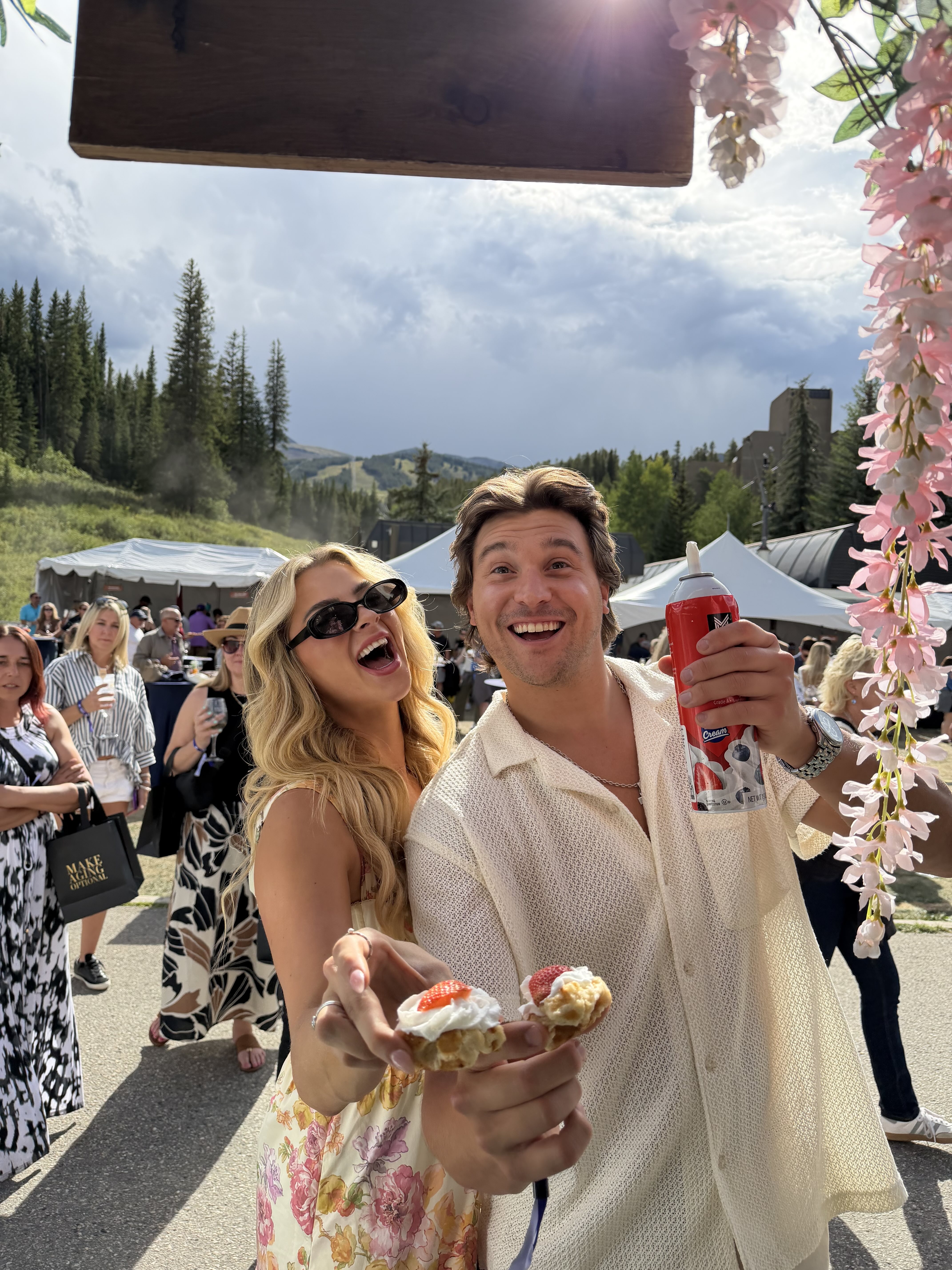 Two guests laughing and holding out waffles with strawberries and cream at an outdoor mountain event