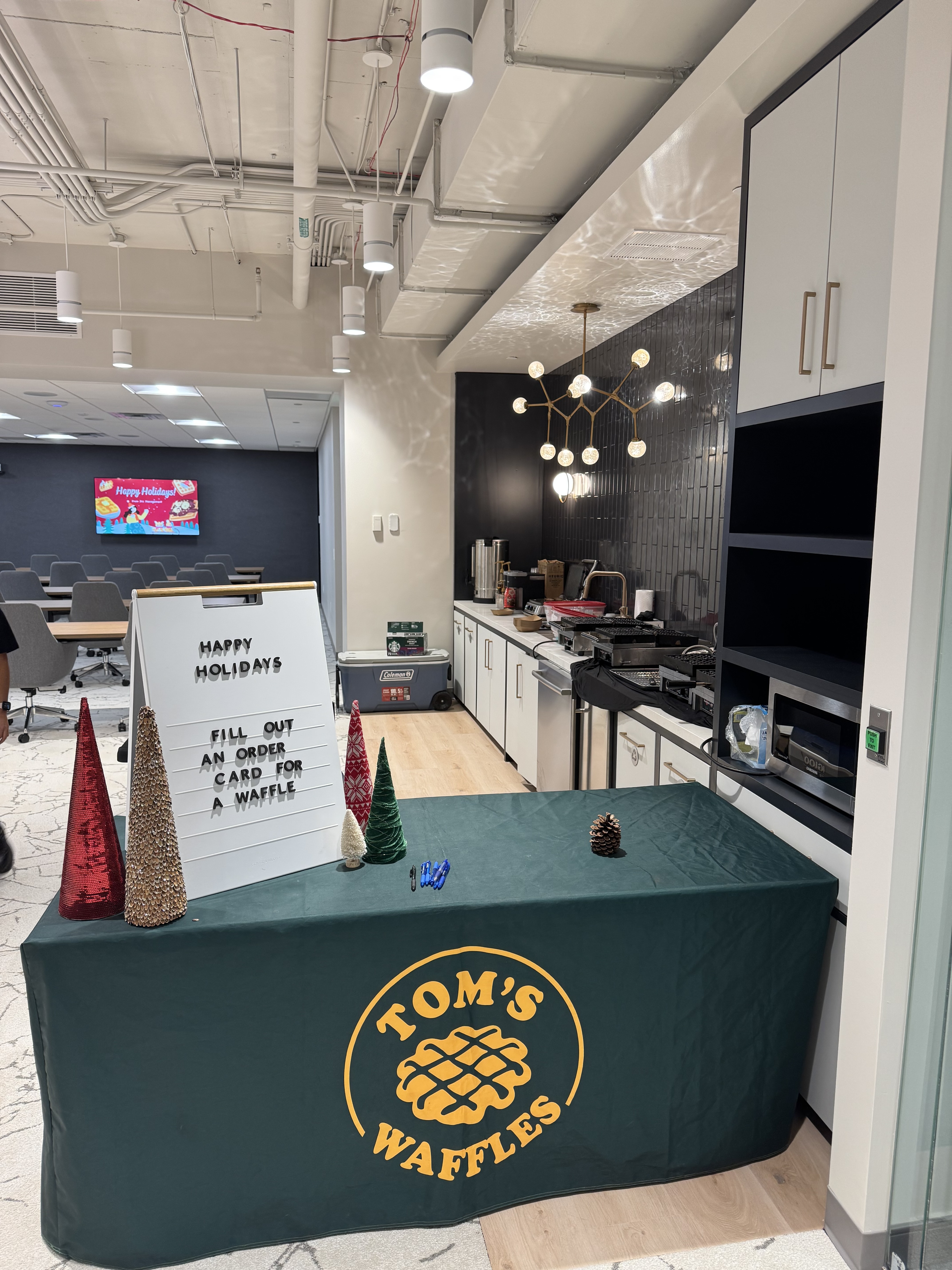 Our table set up beside an office kitchen for a holiday event, with a Happy Holidays sign and small decorated trees