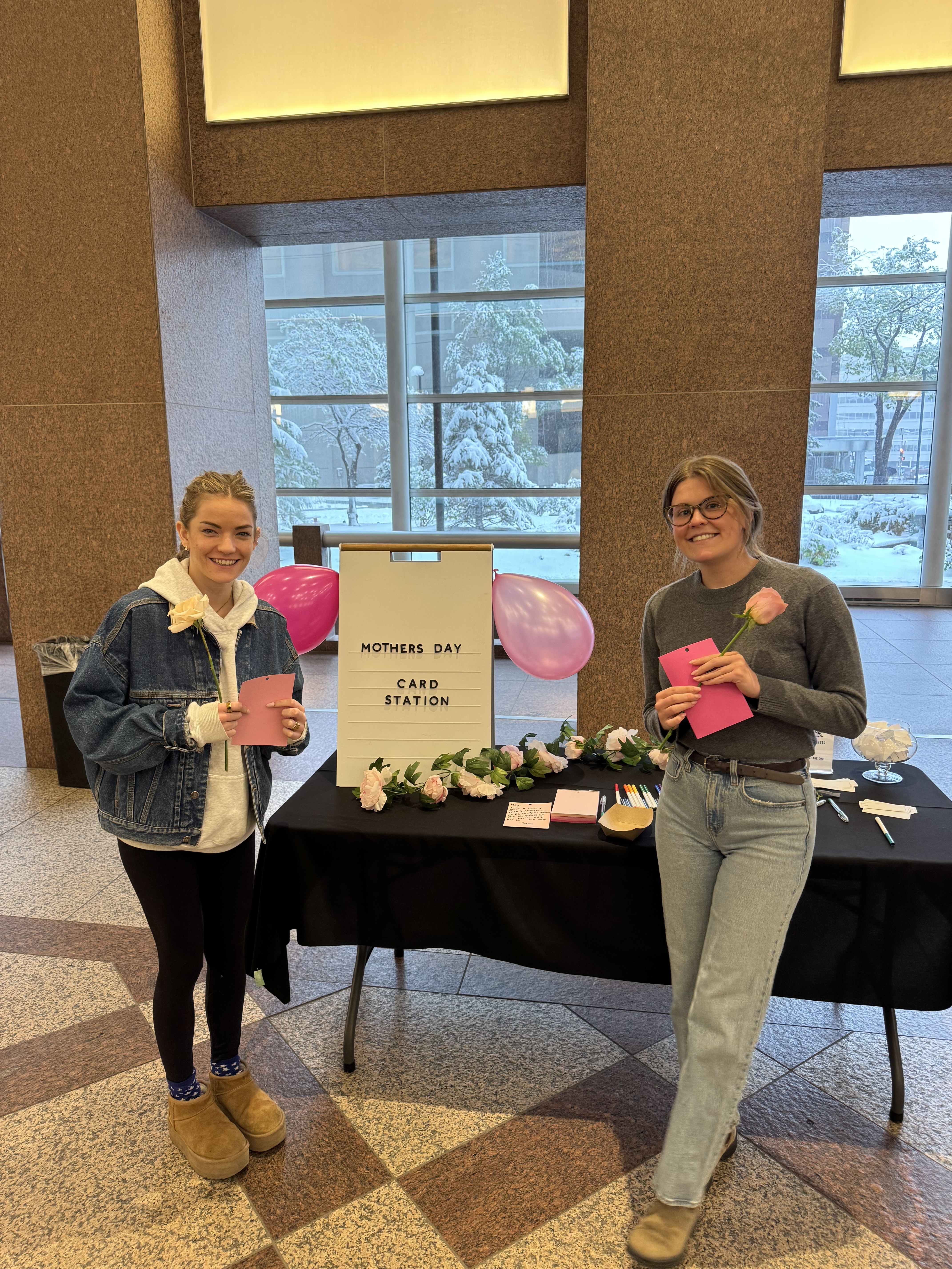 Two guests holding roses and cards at our Mother's Day card station in an office lobby