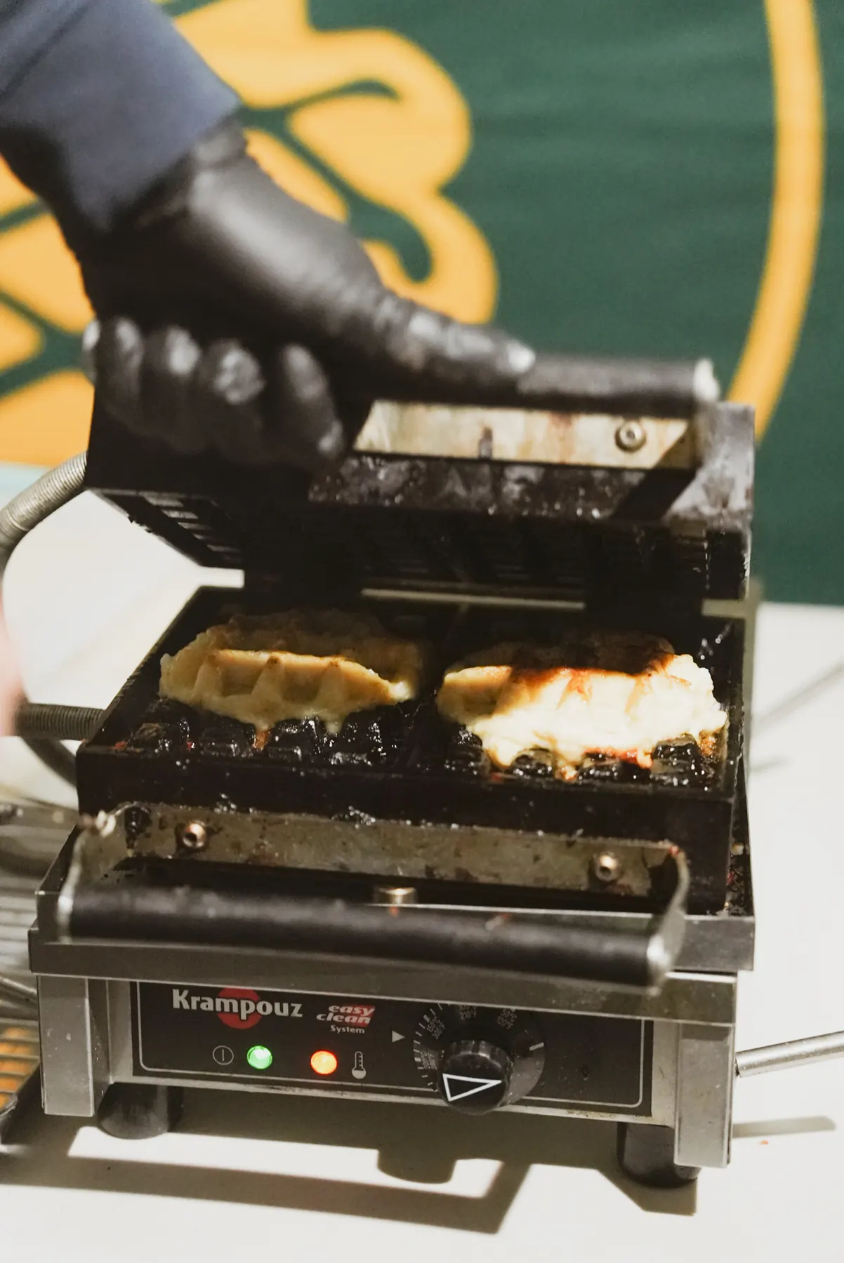 A gloved hand lifting the lid of a waffle iron on two waffles