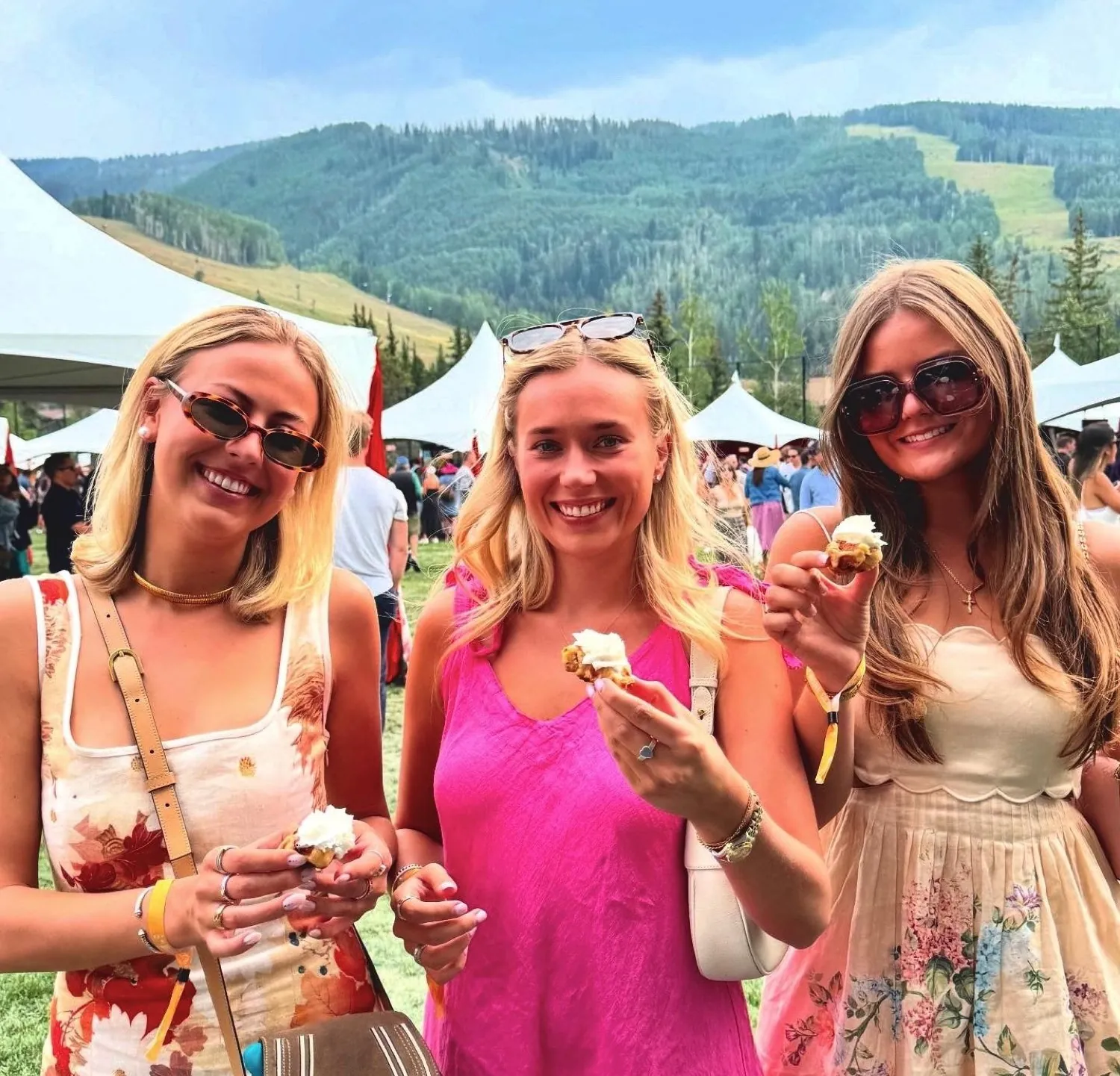 Three guests in summer dresses holding waffles outdoors, with mountains behind