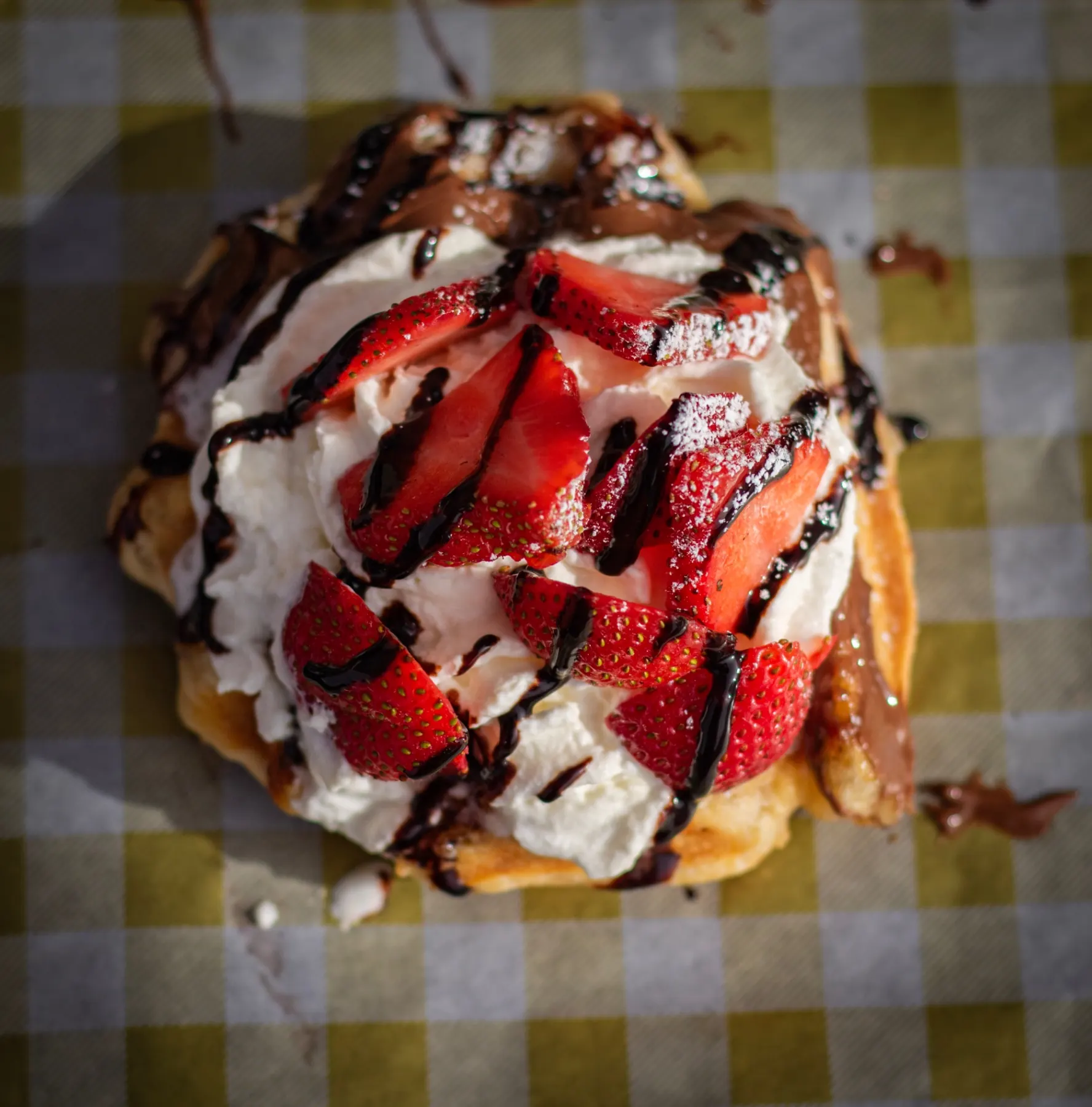 A Liège waffle topped with strawberries, whipped cream and chocolate drizzle