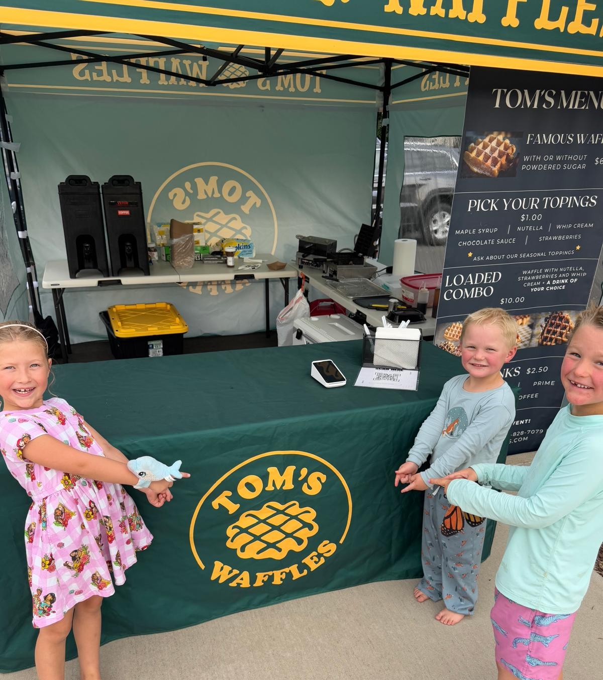 Three kids pointing at the Tom's Waffles table under our tent
