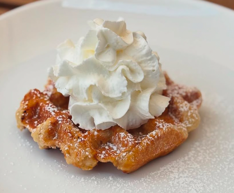 A Liège waffle dusted with powdered sugar under a swirl of whipped cream